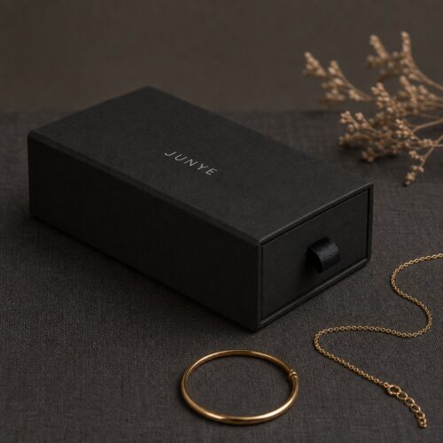 Black long drawer jewelry box styled with a gold bangle and a chain necklace, luxury jewelry packaging scene