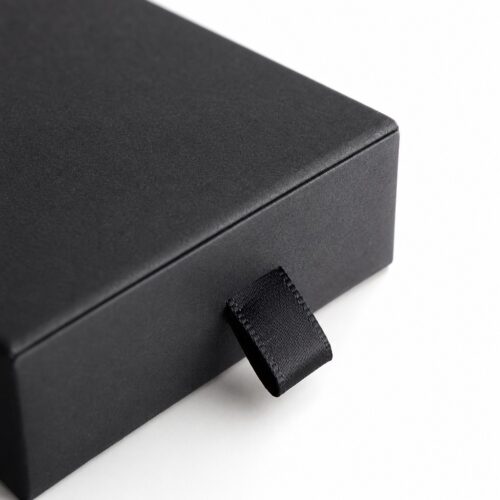 Close up of the slim woven ribbon pull on the front face of a black drawer jewelry box