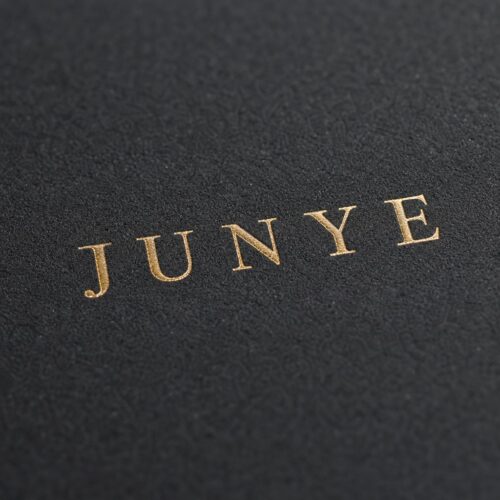 Macro of the gold foil JUNYE logo stamped on matte black specialty paper