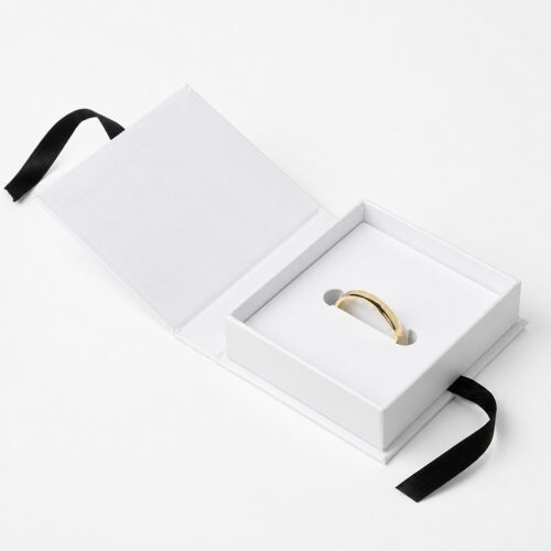 White flip lid jewelry box open on its hinge, holding a gold ring in a cut tray slot