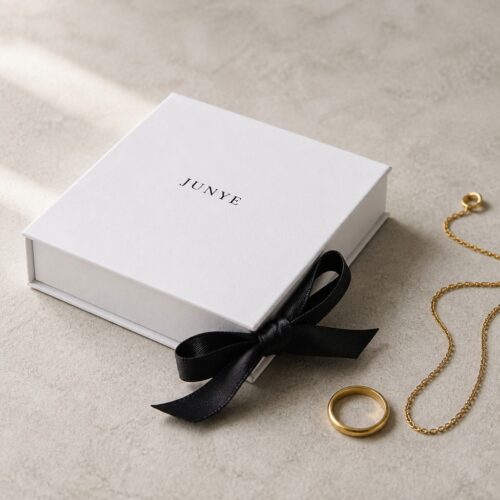 White magnetic flip jewelry box styled with a black bow, a gold ring and a fine chain