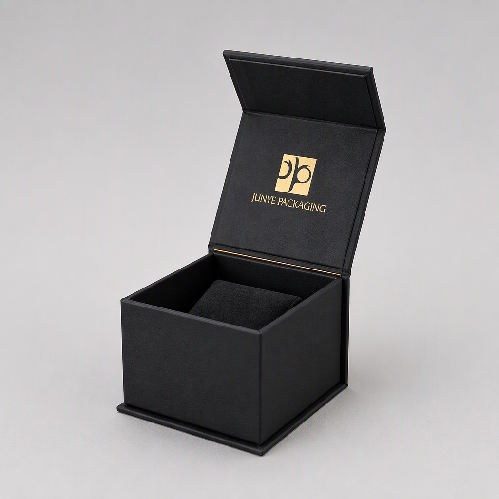 Black cube jewelry box with the magnetic flap lid open on its paper hinge, inner lid mark visible