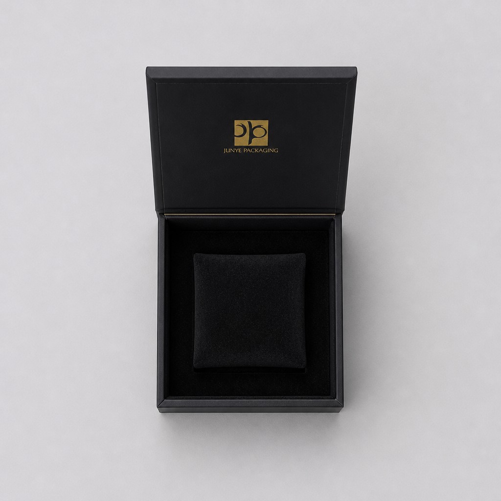 Black cube jewelry box with the magnetic flap lid open, showing the flocked tray and the inside lid mark
