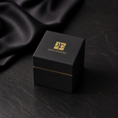 Black cube jewelry box styled on a dark stone surface beside folded black silk