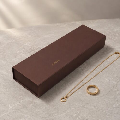 Long brown gift set jewelry box styled on stone with a gold chain and ring beside it