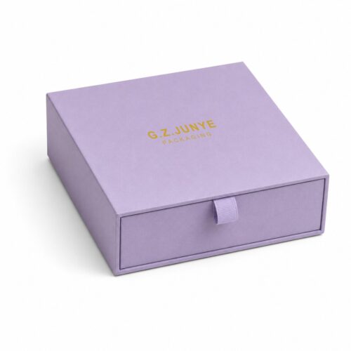 Closed purple drawer box at three quarters, gold foil G.Z.JUNYE PACKAGING block on the sleeve top and the flat loop pull at the tray face
