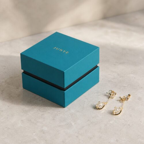 Teal rimmed lid and base jewelry box styled on stone with a gold ring and chain