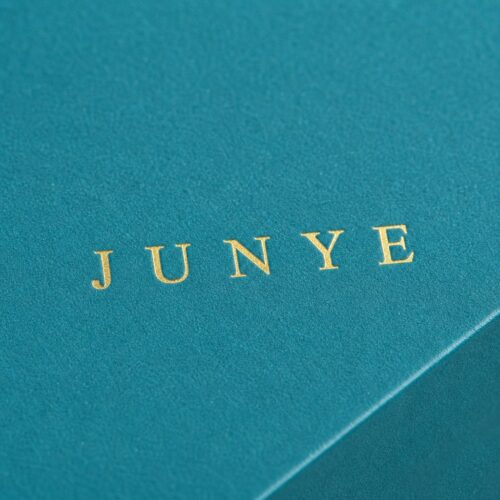 Close up of the gold logo stamped on the teal specialty paper wrap of a rimmed lid box